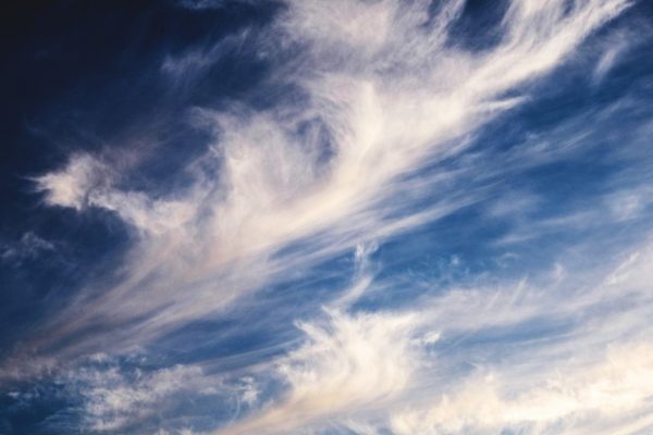 Wispy white clouds stretch across a deep blue sky, creating a dynamic, airy pattern.