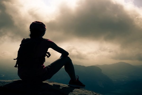 a person's silhouette sitting on a ledge looking out at a cloudy sky