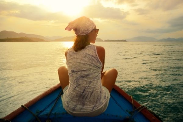 Person on a boat at sunset, gazing at the ocean and distant mountains.