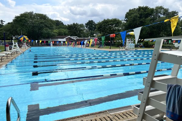 Outdoor swimming pool with swim lanes, lifeguard chair, and colorful flags hanging above the water.