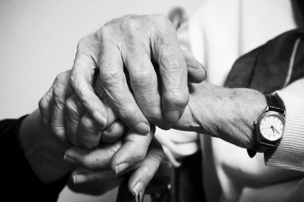 Black and white image of two elderly hands clasped together, symbolizing connection and support.