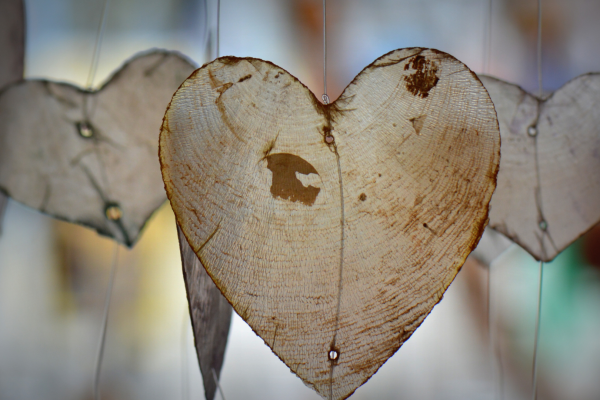 A close-up of heart-shaped wooden ornaments hanging on strings with a blurred background.