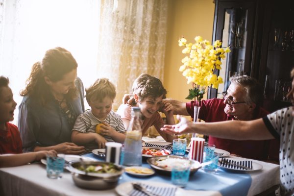 A family with children laughing and dining together at a table set with food and drinks.