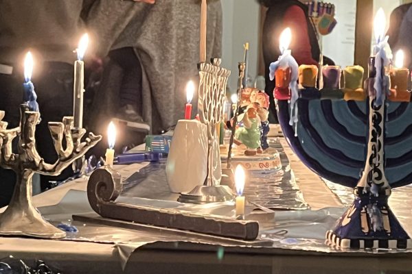 Menorahs and lit candles on a table, celebrating Hanukkah with festive decorations in the background.