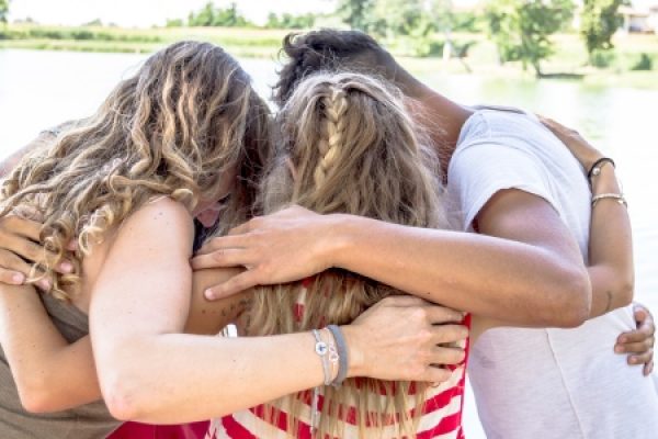 Four people with their arms around each other facing a lake, showing camaraderie and unity.