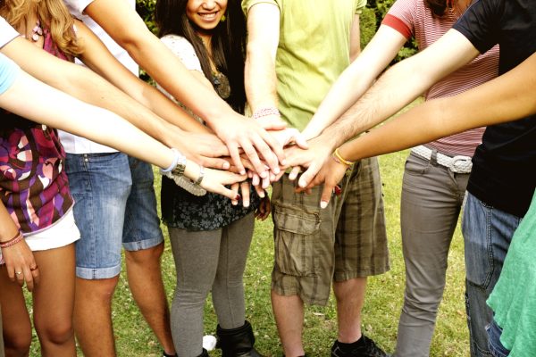 A group of people standing in a circle, stacking their hands together in an outdoor setting.