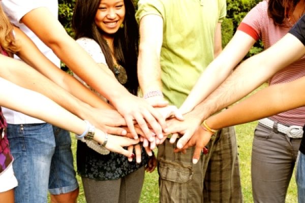 A diverse group of people putting their hands together in a show of unity and teamwork outdoors.
