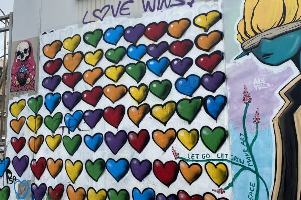 Colorful heart mural with LOVE WINS! written above, on a city wall with various graffiti and street art.