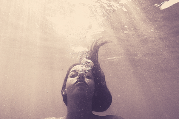 sepia toned photo of woman submerged in water with light filtering from above