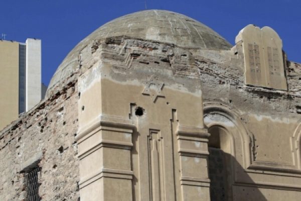 A historic synagogue with a worn exterior, featuring a Star of David and tablets, under a clear blue sky.