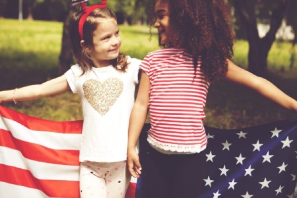 Two girls smiling and holding an American flag in a park.