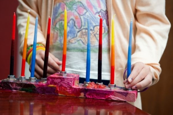 Person lighting colorful candles on a vibrant, artistic menorah.