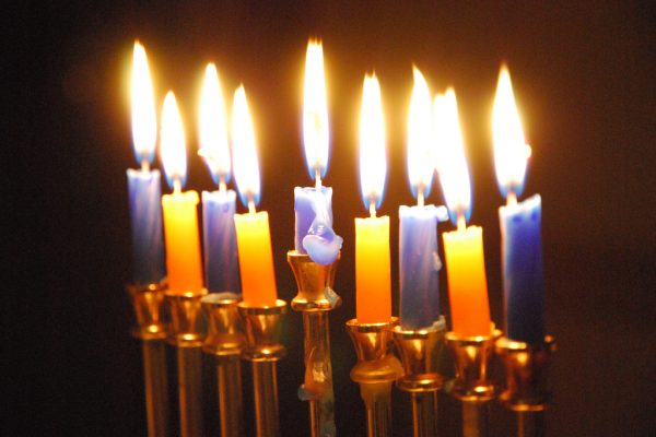 Hanukkah menorah with nine lit candles, in an alternating pattern of blue and yellow, glowing in the dark.