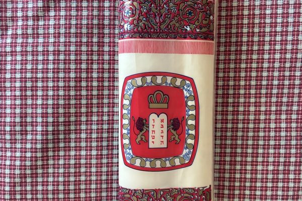 A decorated Torah scroll with red designs lies on a red and white checkered cloth.