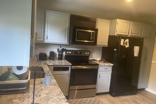 Modern kitchen with stainless steel appliances, black fridge, marble counters, and light gray cabinets.