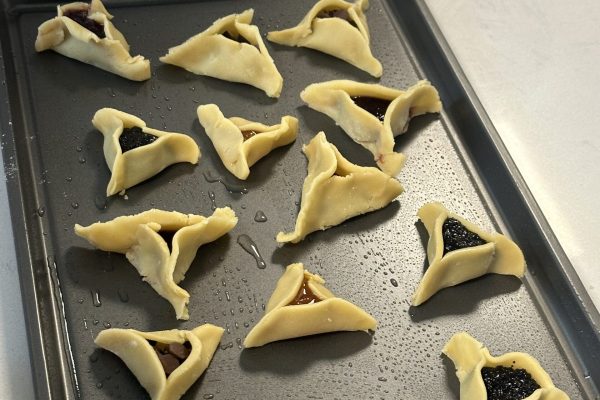 Unbaked hamantaschen cookies with various fillings on a baking tray, ready to be baked.