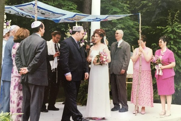 a couple stand under a chuppah surrounded by family and friends