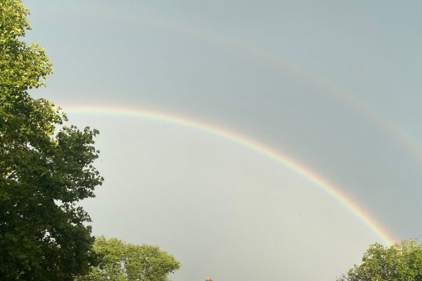 A double rainbow arches across the sky above green trees.
