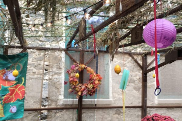 Outdoor pergola decorated with hanging lights, a wreath, a purple lantern, and autumn-themed banners.