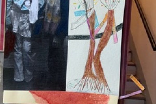 Black and white photo of two people beside a colorful tree drawing on a wall.