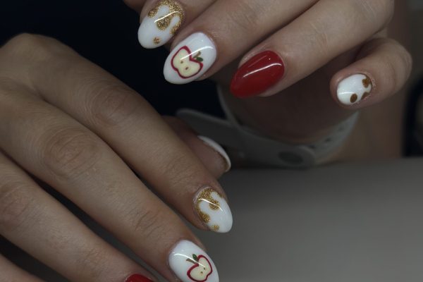hands with painted nails: pinkies and pointer fingers are white with sparkly gold drip, ring fingers are all red, middle fingers have white background with apples that are cut open, thumbs have white backgrounds with red apples