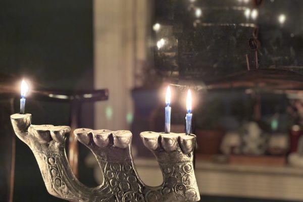 A menorah with two lit candles stands on a table, with a blurred background and mirror reflection.