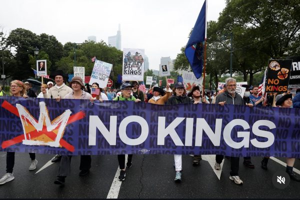 People march holding a large NO KINGS banner with a crossed-out crown symbol on a city street.