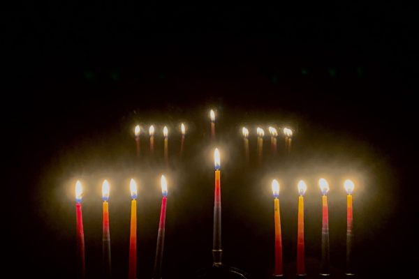 fully lit hanukkiyah in the dark with another hanukiyah in the background that appears to be a reflection of the first