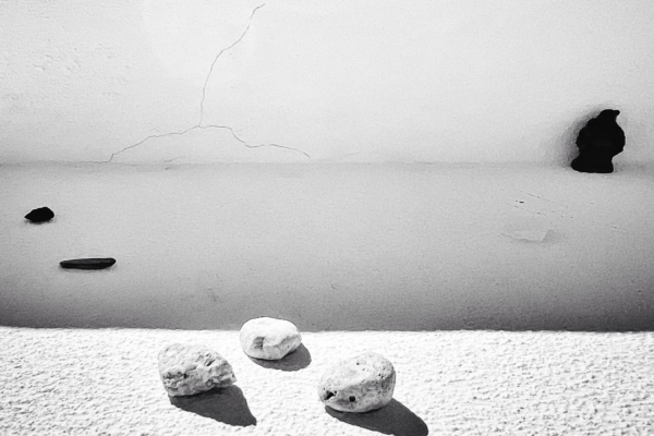 Three small stones on a textured ledge with a cracked, shadowed wall and two holes in the background.