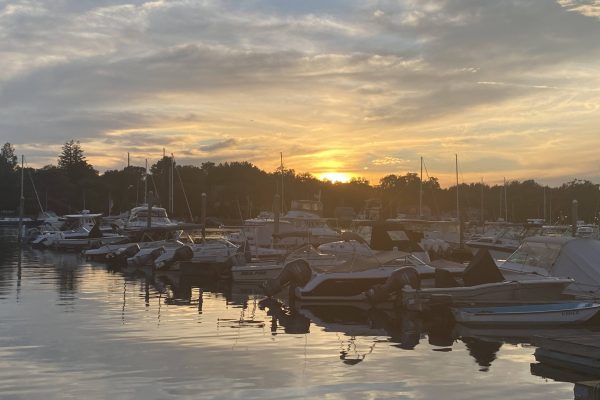 Boats docked at a marina with a colorful sunset and reflections on the water.