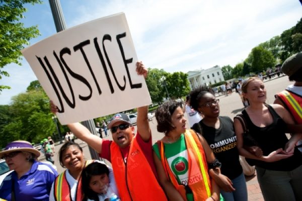 People holding a Justice sign during a rally near a large white building.