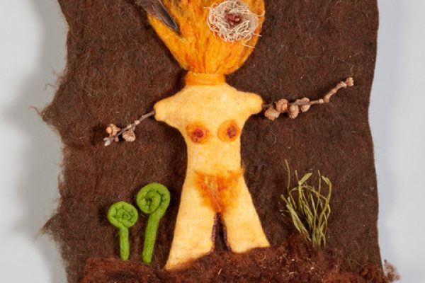 Textile art of a female figure with fiery hair, twig arms, and plants on a brown fabric background.