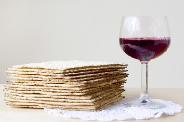 Stack of matzah next to a glass of red wine on a white lace doily.
