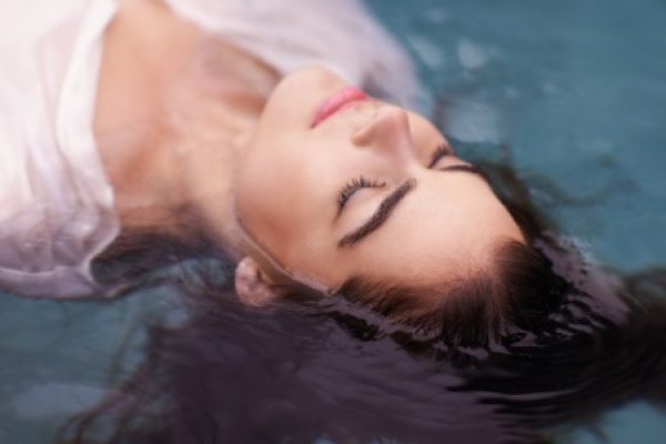 A person floating peacefully in water with eyes closed, wearing a white garment.