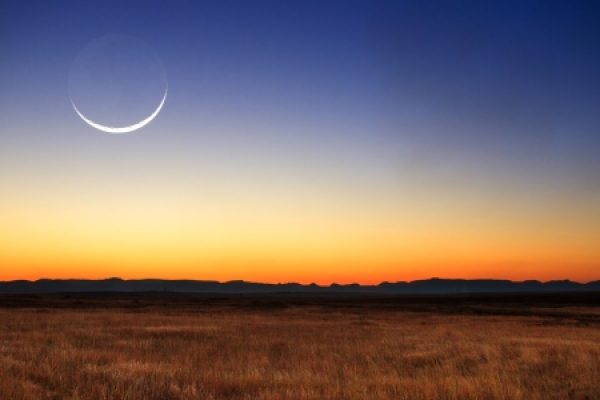 Crescent moon and gradient sunset sky over a vast, grassy plain with distant mountains.