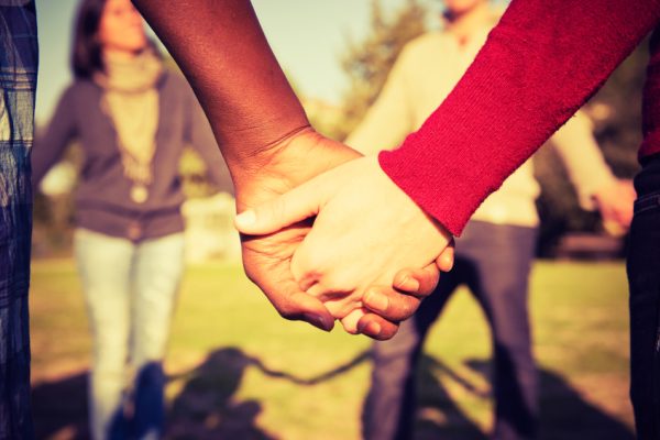 a black-skinned had and white-skinned hand hold hands