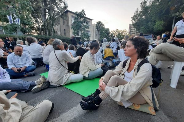 Rabbi Haviva dressed in white sits with protestors