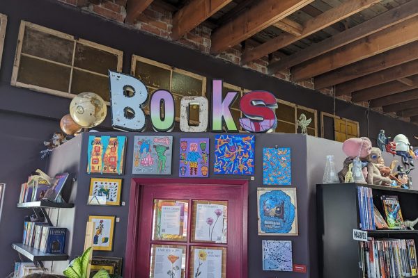 Colorful Books sign above bookshelves, surrounded by art, books, and unique objects in a cozy bookstore.