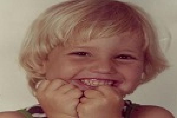 A smiling child with blond hair and hands held close to their face.
