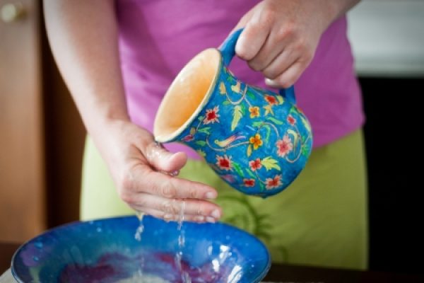 Person pouring water from a floral jug over a hand above a blue bowl.