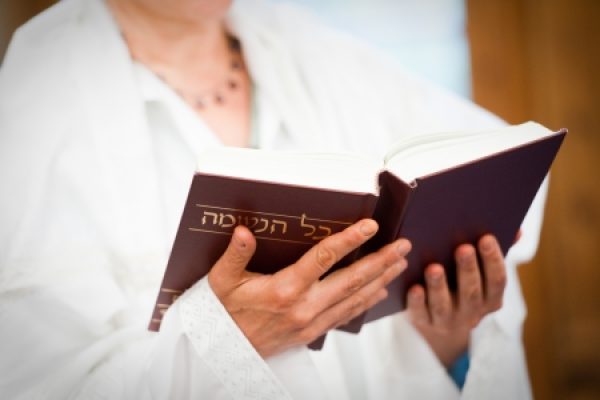 A person wearing white holds and reads a Hebrew book.