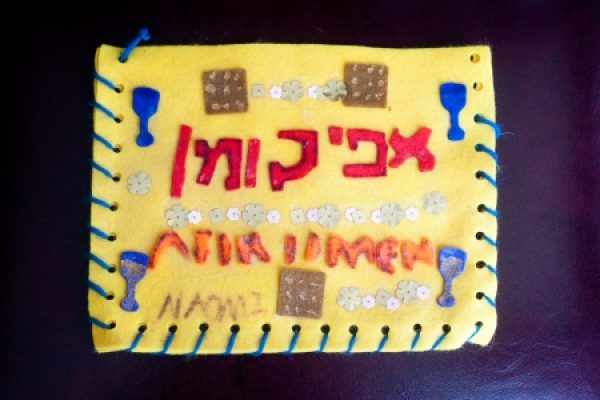 Colorful handmade matzah cover with Hebrew letters and decorative symbols on yellow felt.