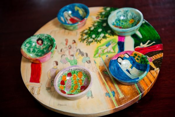 Colorful hand-painted bowls on a round, illustrated wooden platter with vibrant scenes.