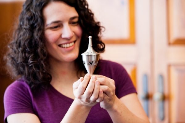 A person smiling and holding a metal dreidel.