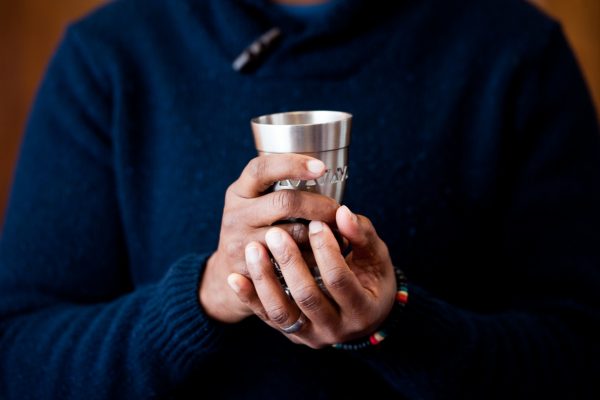 Person in a blue sweater holding a silver cup with both hands.