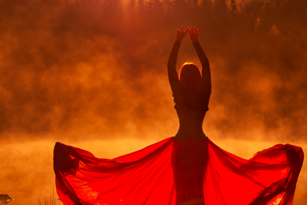 woman in flowing red skirt silhouetted against a forest sunset