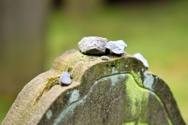 Stones placed on top of a mossy tombstone in a cemetery.