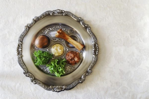 Seder plate with symbolic Passover foods: bone, egg, herbs, charoset, bitter herbs, and horseradish on ornate platter.