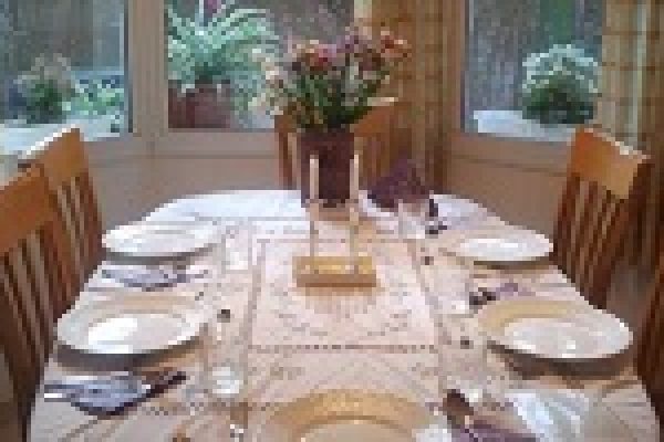 A dining table set for six with white plates, glasses, and a floral centerpiece near large windows.