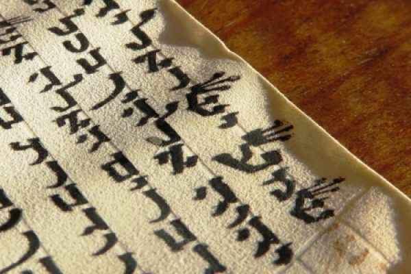 Close-up of ancient text written in Hebrew on aged parchment, with a wooden surface in the background.